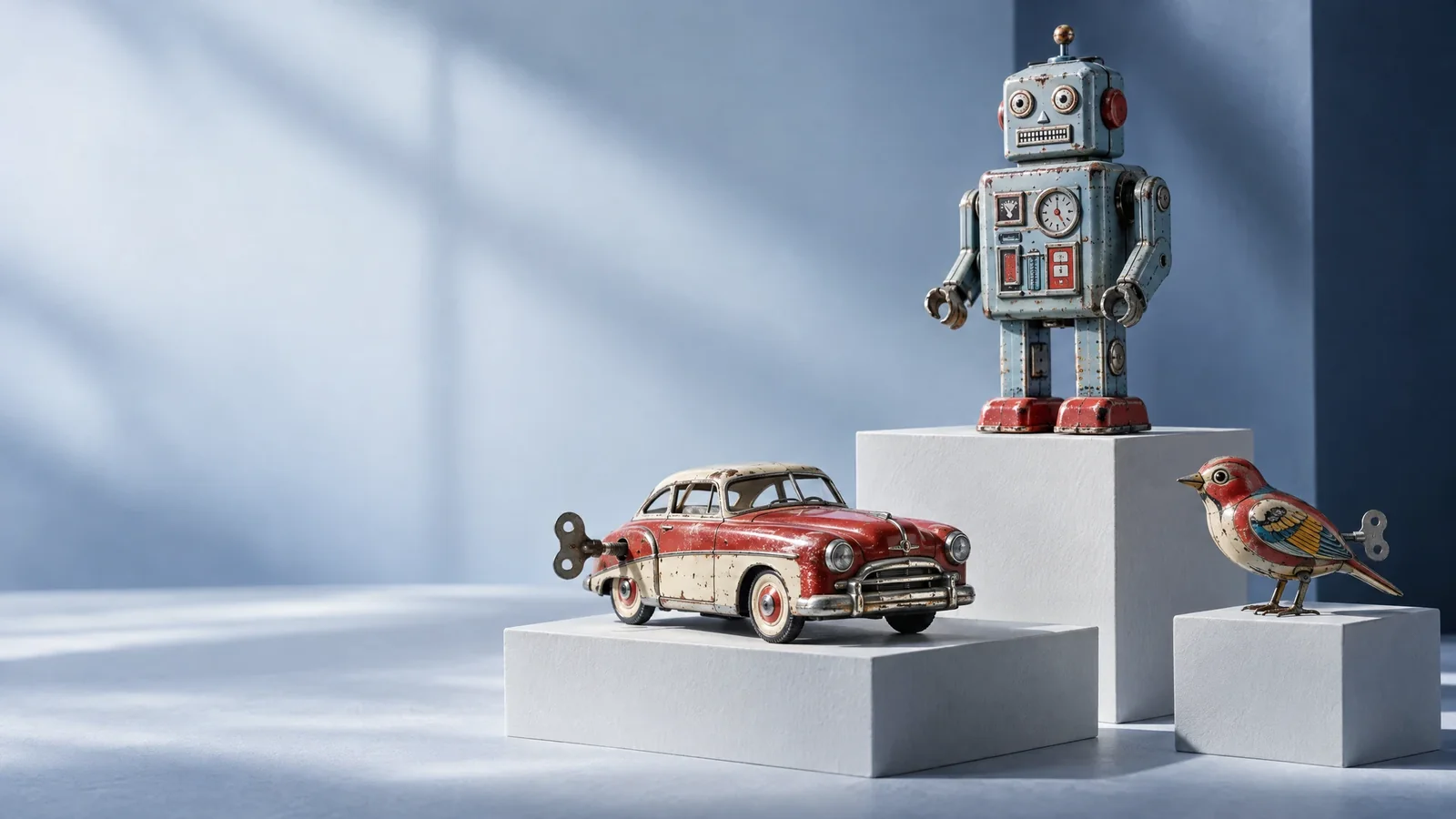 Illustrative still life of a vintage-style toy robot, a miniature car and a mechanical bird on pale blue display plinths.